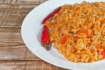 Pilaf with meat, peppers and carrots in a white plate. Rice on a wooden pink board.