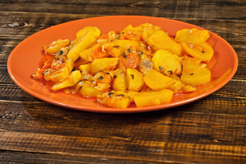 Potatoes in a green plate on a wooden table. Boiled potatoes with orange sauce on a brown board.