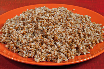 Buckwheat orange plate on a wooden table. Food in utensils on a background of old red plywood.