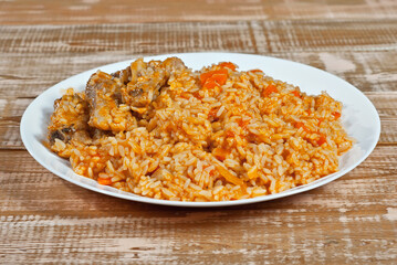 Pilaf with meat and carrots in a white plate. Rice on a pink shabby board.