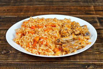 Pilaf with meat and carrots in a green plate. Rice on a brown shabby board.