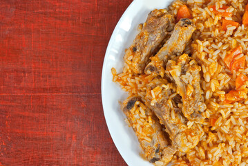 Pilaf with meat and carrots in a white plate. Rice on red plywood. Place for text and copy space near food.