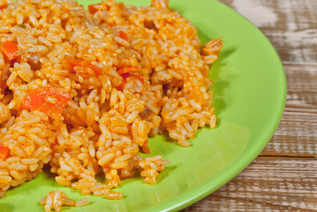 Pilaf with meat and carrots in a green plate. Rice on a pink shabby board.
