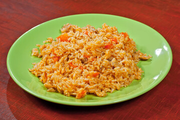 Pilaf with meat and carrots in a green plate. Rice on red plywood.
