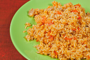 Pilaf with meat and carrots in a green plate. Rice on red plywood.