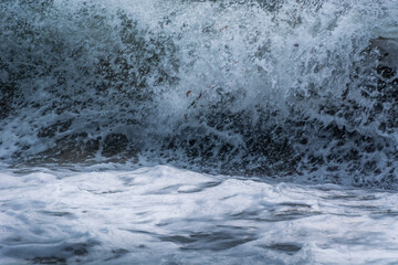 Close up waves hitting shore. Sea water surface with foam and ripples. Natural event
