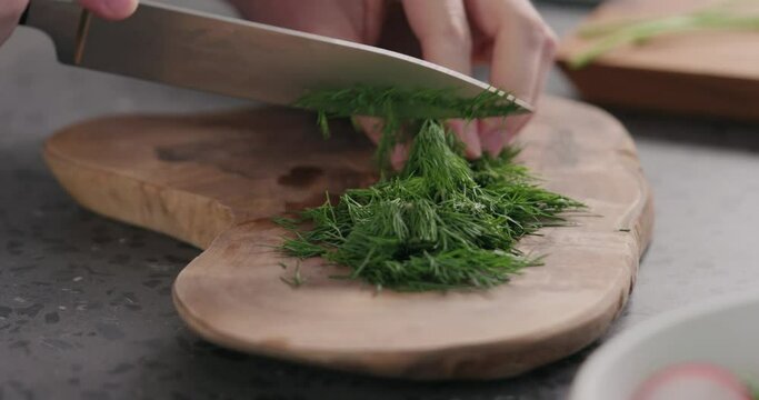 Slow motion man chopping fresh dill on olive board