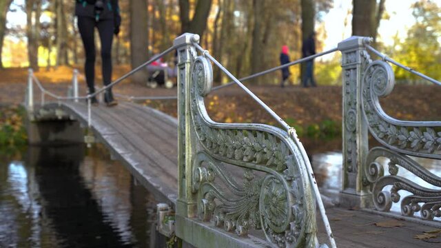 Girl in black walks along small bridge over river with railings in park