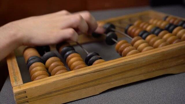 Male hand on vintage wooden bills. Hand making calculations on vintage abacus sliding beads