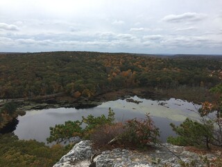 Fototapeta premium View over the edge of a cliff on a mountain on Lantern Hill trail in Connecticut, with a pond below in the distance 