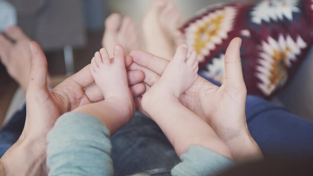 Closeup of father hands holding newborn baby boy legs. Gently parenting, family together.