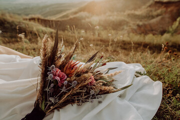 wedding bouquet in boho style collected from wild flowers, the bride holds a bouquet in her hand, in nature, white dress, live plants, a composition of dried flowers