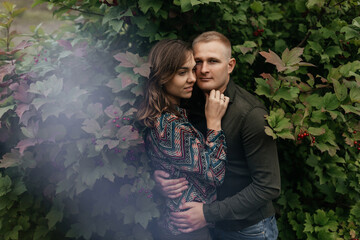 Young man and woman standing and embracing at the background of the green leaves. Happy couple