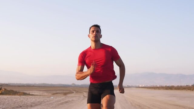 Young male athlete doing running training on beach at sunset