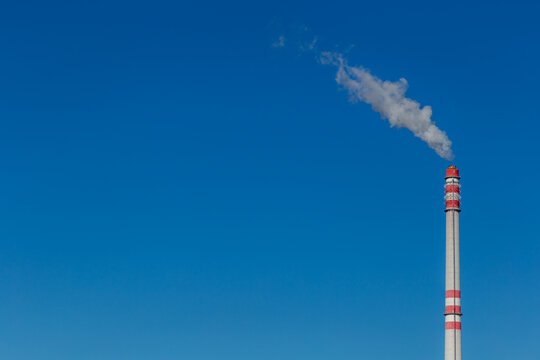 Smoke from a tall chimney in the clear sky, blue background and space for text, ecological theme