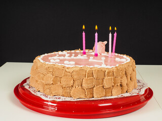 Lit candles on a pink marzipan covered birthday cake, with a rose and beautiful chocolate pattern