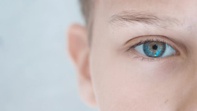 Boy eye looking directly to camera. Half face. Child near grunge gray wall