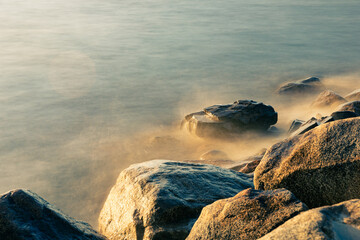 Waves hit the rocks on the beach at sunset