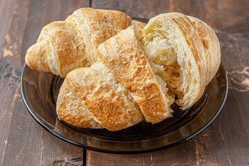 freshly baked flavorful crispy croissants on a glass plate on a wooden table close up