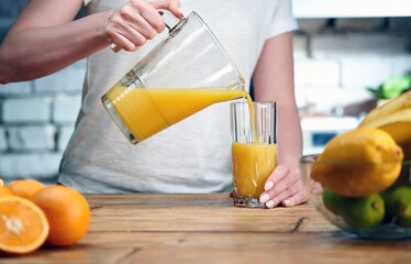Close up of woman's hand holding glass carafe or jug. Drinking orange juice at home in the kitchen....