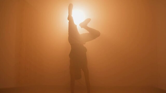 Silhouette of hipster b-boy breakdancing and doing one-hand stunt