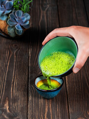 Closeup photo the hand of a professional teamaker holding a bowl of freshly made traditional asian matcha tea. Woman pours matcha green tea into a bowl. Traditional tea ceremony. Dark wood background
