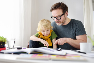 Father helping child do his homework at home. Homeschooling, distance learning, online studying,...