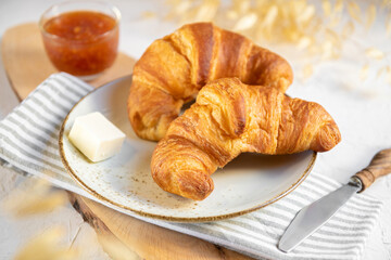 A pair of croissants on ceramic plate with butter and orange jam on a wooden cutten board. Continental breakfast background, close up