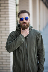 Young bearded man in sunglasses on the street posing on camera walk in the city.