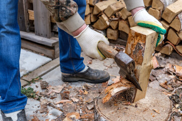 A man cleans the bark from birch wood with a metal ax with a wooden handle. Logging firewood for the fireplace insert.