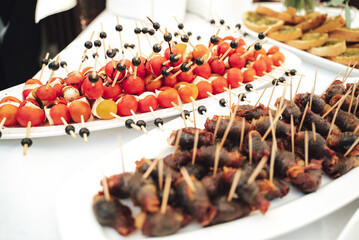 Self-service buffet table with various types of small snacks. Focused on stuffed cherry tomatoes with cheese. Celebration, birthday, party, wedding