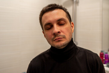 Obraz premium Portrait of a young short haired man wearing black turtleneck with eyes closed on background of light.