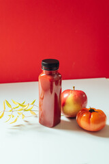 Red smoothie drink in bottle surrounded by red apples and tomatoes