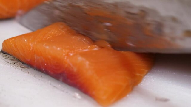Close-up of cutting fresh salmon fillet using a white chopping board. Preparing raw fish steak in the kitchen.