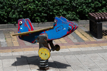 old wooden carousel airplane on the playground in the park. attraction for children. swing with peeling paint. toy wooden plane