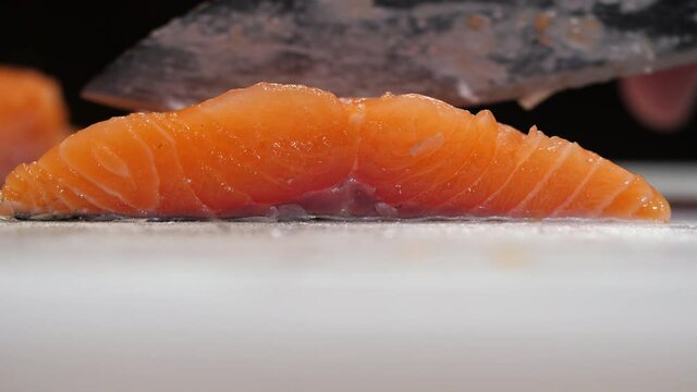 Side view of slicing raw salmon fish fillet on a white chopping board. Cutting fresh fish steak at home.