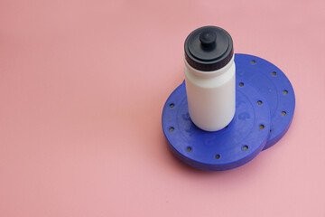 online SPORTS at home, during self-isolation, keep your figure in shape, on a pink background is a white water bottle and disks with dumbbells