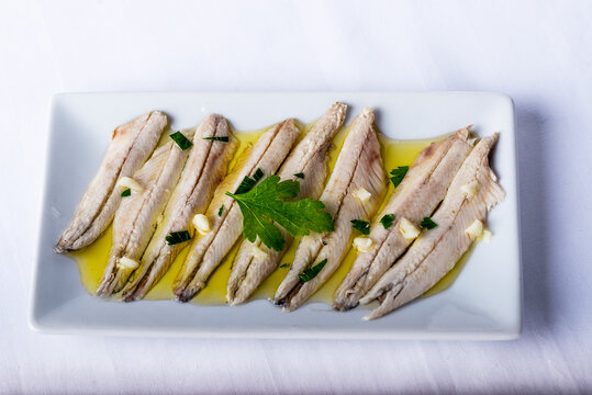 anchovies in vinegar with garlic and parsley on a white background and surrounded by ingredients.