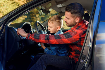 handsome father pointing on something while teaching teen son driving car