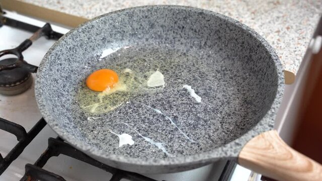 Chef lifts a frying pan with an egg over the gas stove. Cooking egg in a frying pan over an gas burning stove
