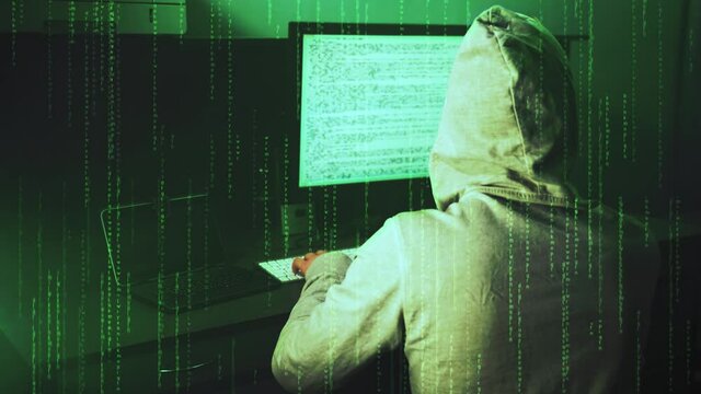 Teenage hacker in hoody works on desktop computer. Data code on display screen