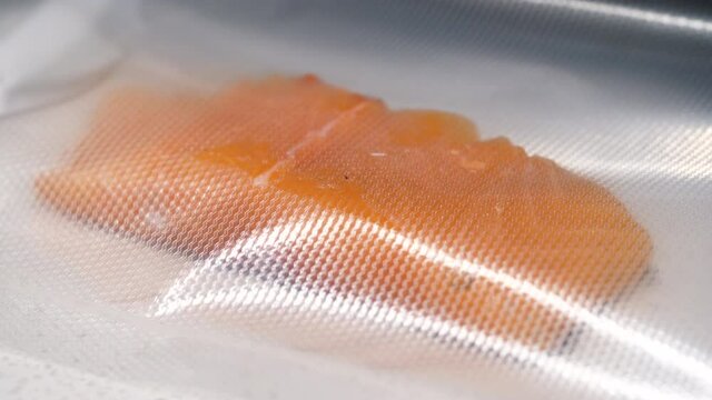 Vacuum packing machine sealing a raw salmon fish fillet in the kitchen.