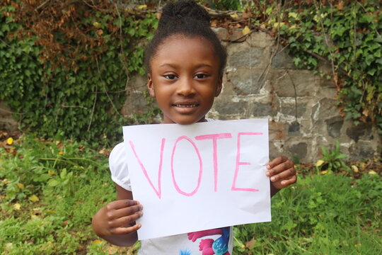 Young child holding white paper sign with word Vote written in Pink letters 