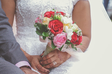 Indian couple's hands holding a beautiful wedding bouquet red and pink roses