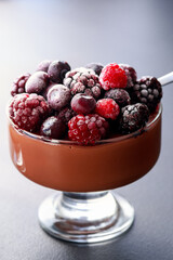 chocolate mousse dessert with frozen berries on grey background close up