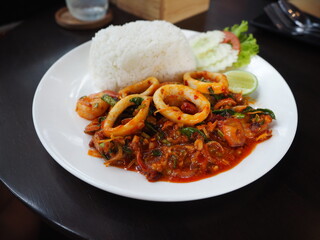 stir fried squid with Thai style hot and spicy sauce with herb (Tom yum paste) with cooked rice on white dish on table