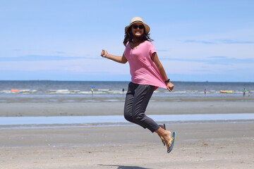 Asian women wearing pink shirts and wooden hats are jumping with joy and freshness. On the beach on a summer holiday Summer concept