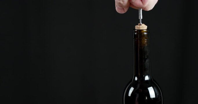 Male hand with corkscrew removes cork from bottle of wine.