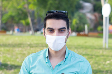 Portrait of young man wearing medical mask posing in sunny park