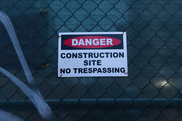 A construction site sign is tagged to a green mesh tarp that's covered in graffiti. The sign warns passerby's trespassing is not allowed and the site is dangerous.